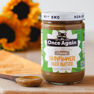 Jar of Once Again Sunflower Butter on a table with some sunflowers